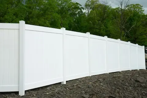 Tall white vinyl privacy fence installed along a cleared residential property line