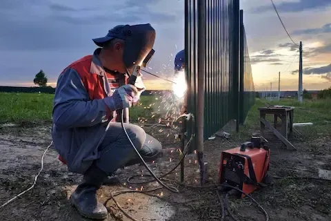 Certified welder fabricating a custom metal fence on-site during a commercial installation