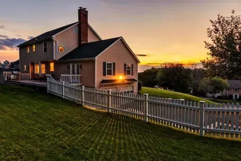 Two-story home at sunset with a freshly installed white picket fence in the front yard