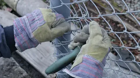 Worker in leather gloves repairing a damaged section of chain link fence