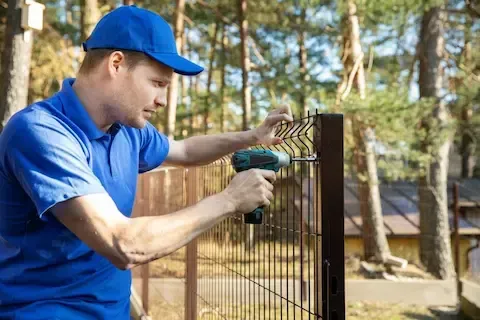 Fence installer in uniform securing a black welded wire fence panel to a steel post