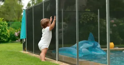 Toddler standing safely behind a black mesh pool safety fence in a backyard
