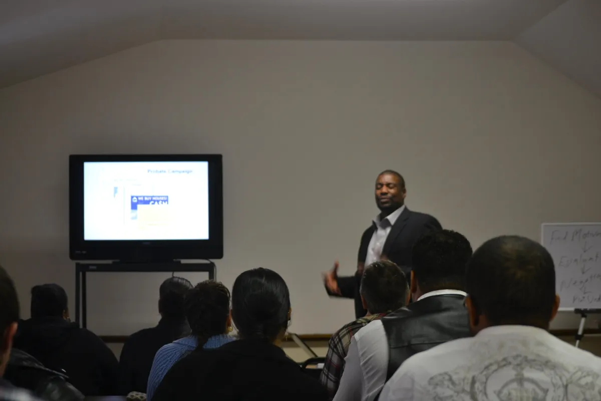 Terence Young delivering a live real estate training session to a room of attendees, with a presentation slide titled 'Probate Campaign' displayed on a monitor. Audience is engaged, showcasing Terence’s hands-on teaching style and classroom authority.