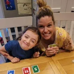 Mum and daughter playing cards at a table in a kitchen. Both are leaning forward and smiling..