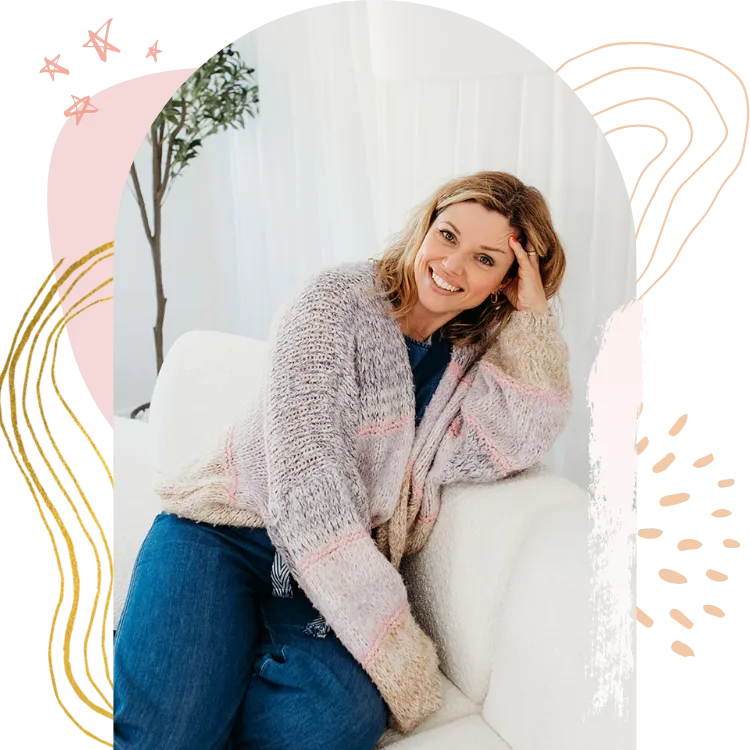 Laura sat on sofa, leaning on her arm. Denim jumpsuit and woollen pastel shade pink and purple knitted cardigan. Chronic illness mums and business.