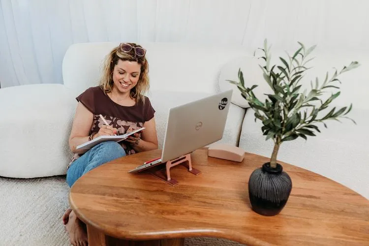 laura fox chronic illness mums business coach writing in a dairy, laptop in front of her on a wooden table
