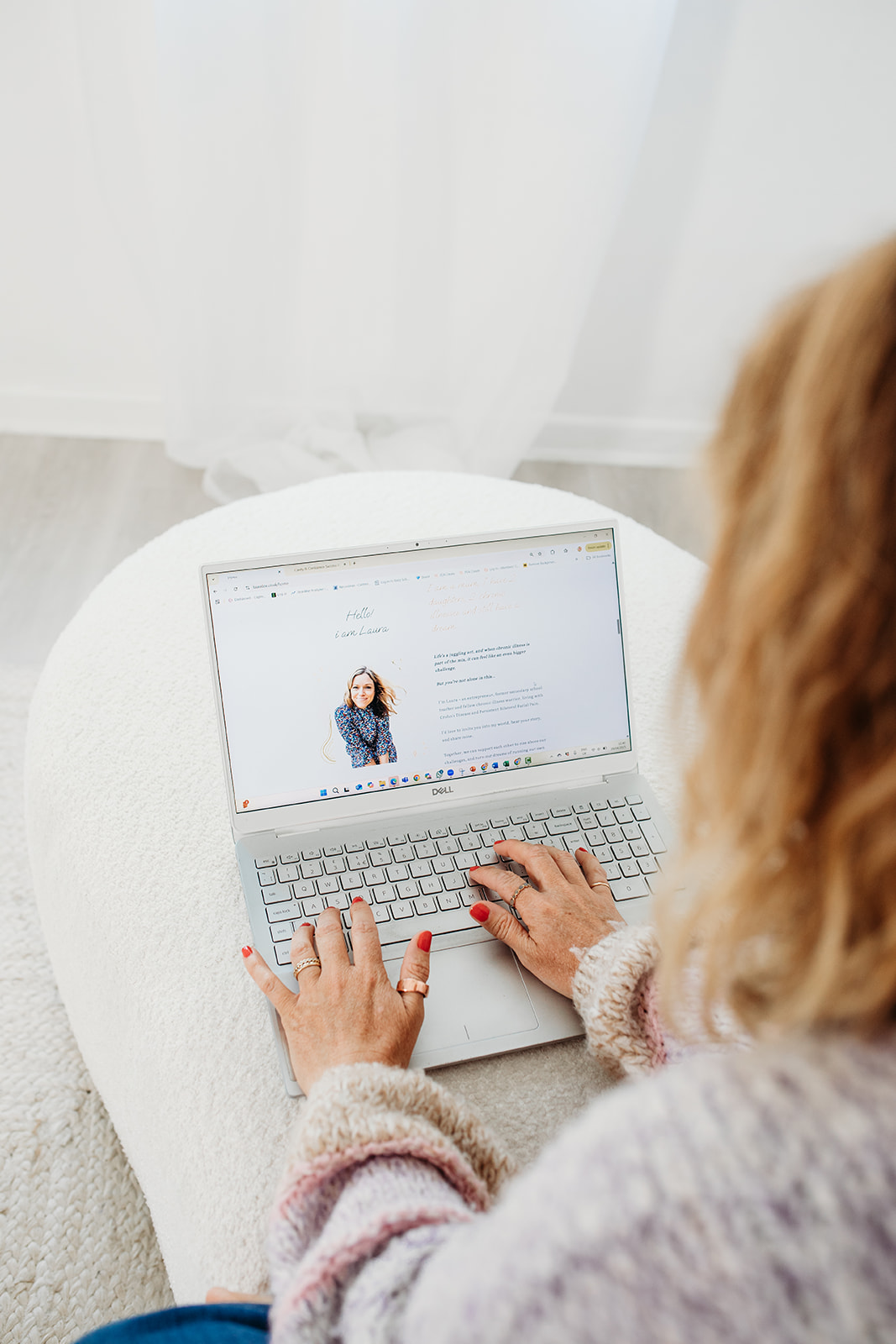 Laura Fox holistic business coach, on a white sofa with her laptop, looking at the screen. Building a fully booked business with part-time energy