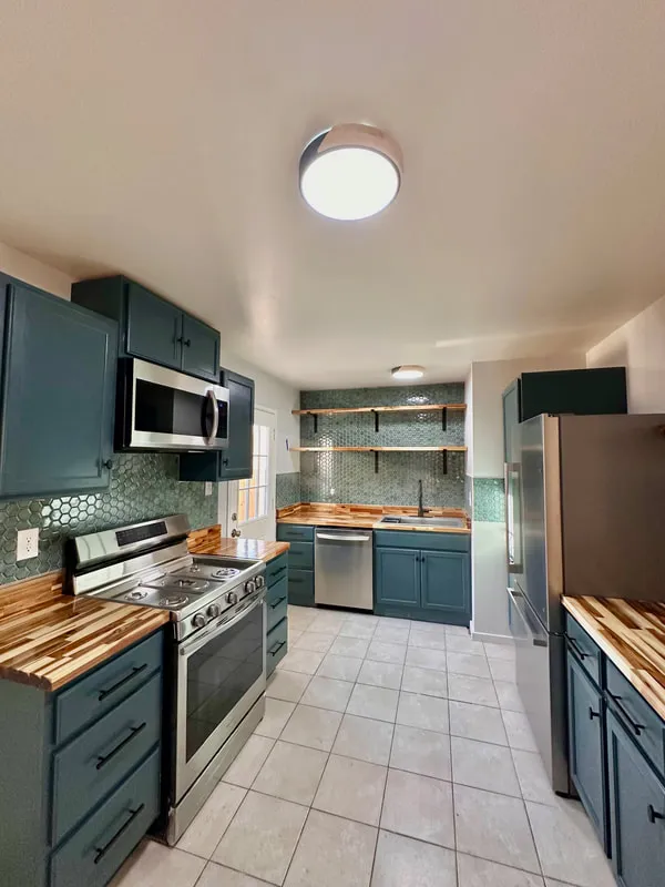 Renovated kitchen with teal cabinets, wood countertops, and stainless steel appliances