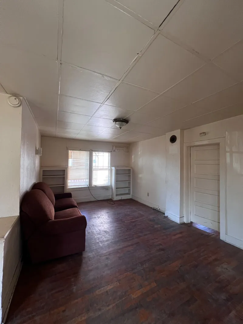 Living room before renovation, with dark flooring and a paneled ceiling