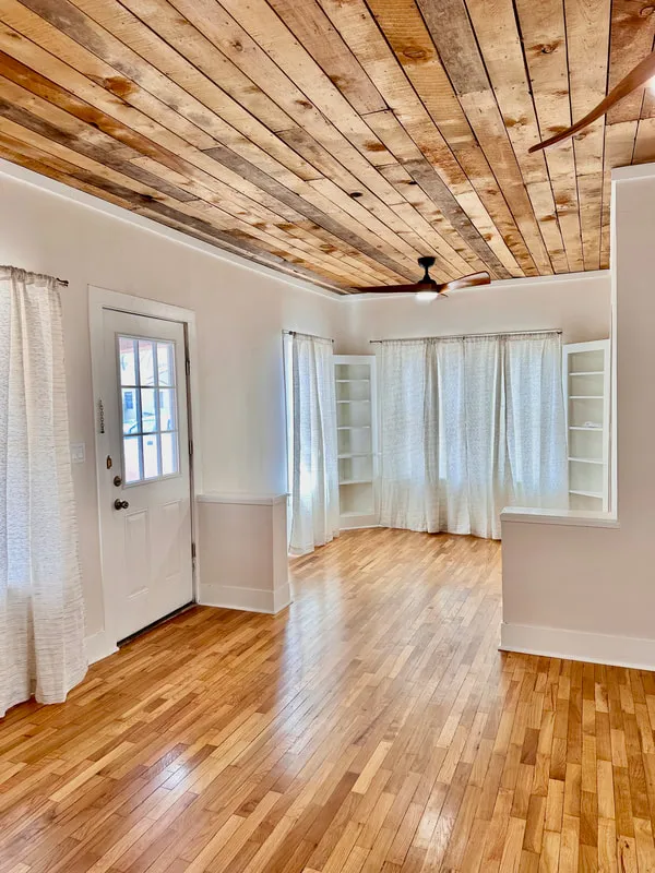 Renovated living room with wood flooring, a wood-plank ceiling, and white curtains