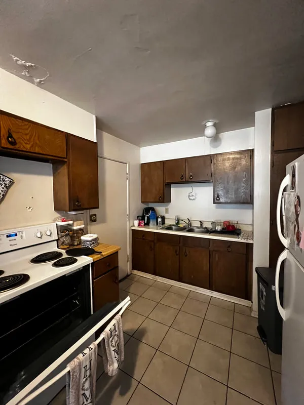Kitchen before renovation, with dark wood cabinets and white appliances