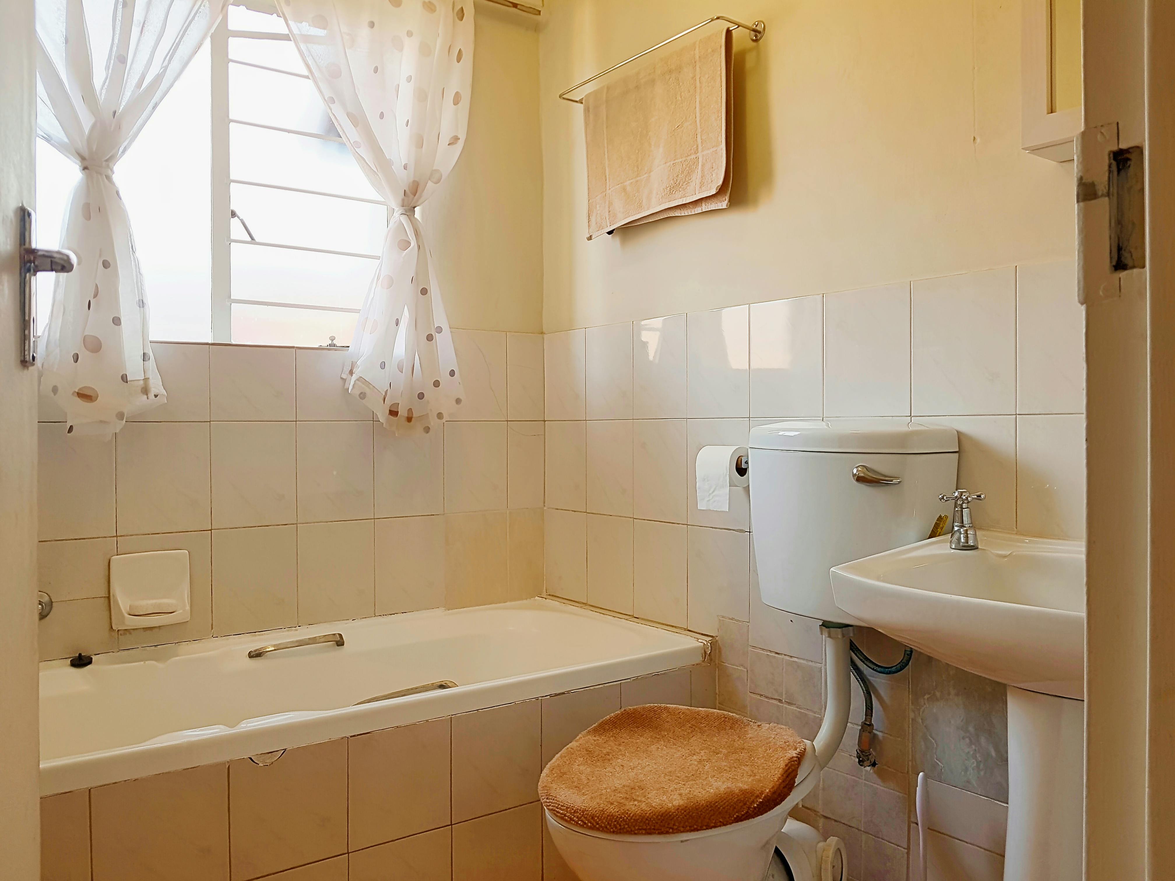 1990s style bathroom with beige ceramic tiles, bathtub and toilet
