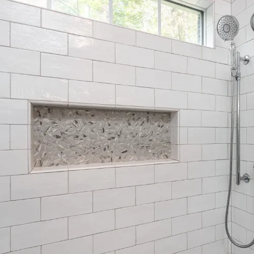 Elegant walk-in shower featuring frameless glass doors, luxurious marble tile, and a rainfall showerhead for a spa-like experience. Built-in niches provide stylish storage, while soft lighting enhances the modern, serene ambiance of this expertly remodeled bathroom.