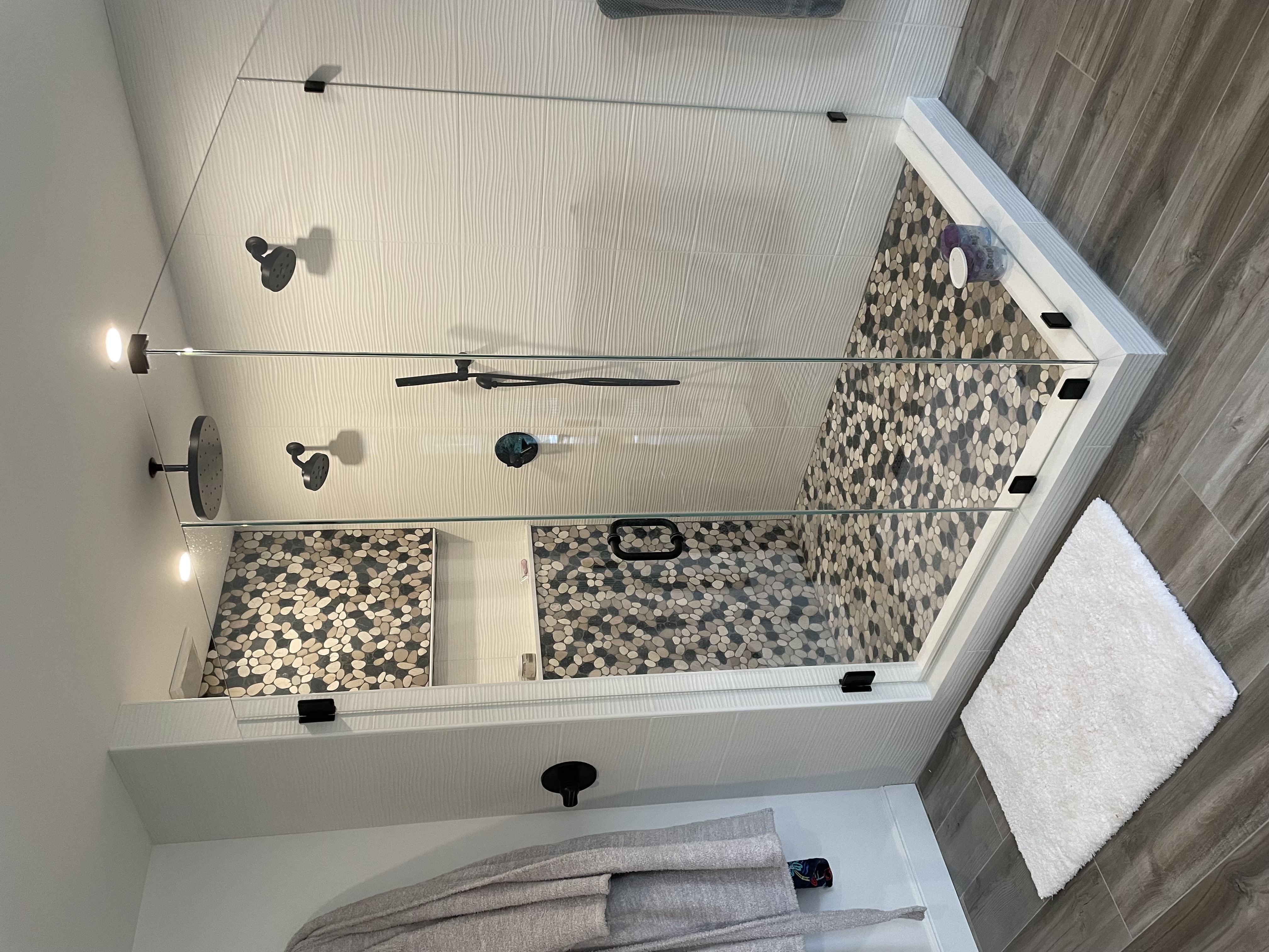 Large custom tile shower by Grams Tile in central Massachusetts — two-person walk-in shower with pebble mosaic accent wall, textured wave tile, matte black fixtures, and frameless glass enclosure