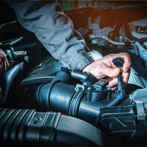 Shows a mechanic working on an engine compartment, specifically handling a sensor or connector. 