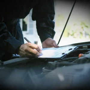 Mechanic performing a pre-purchase vehicle inspection with a checklist under the car hood to ensure safety and reliability before buying.