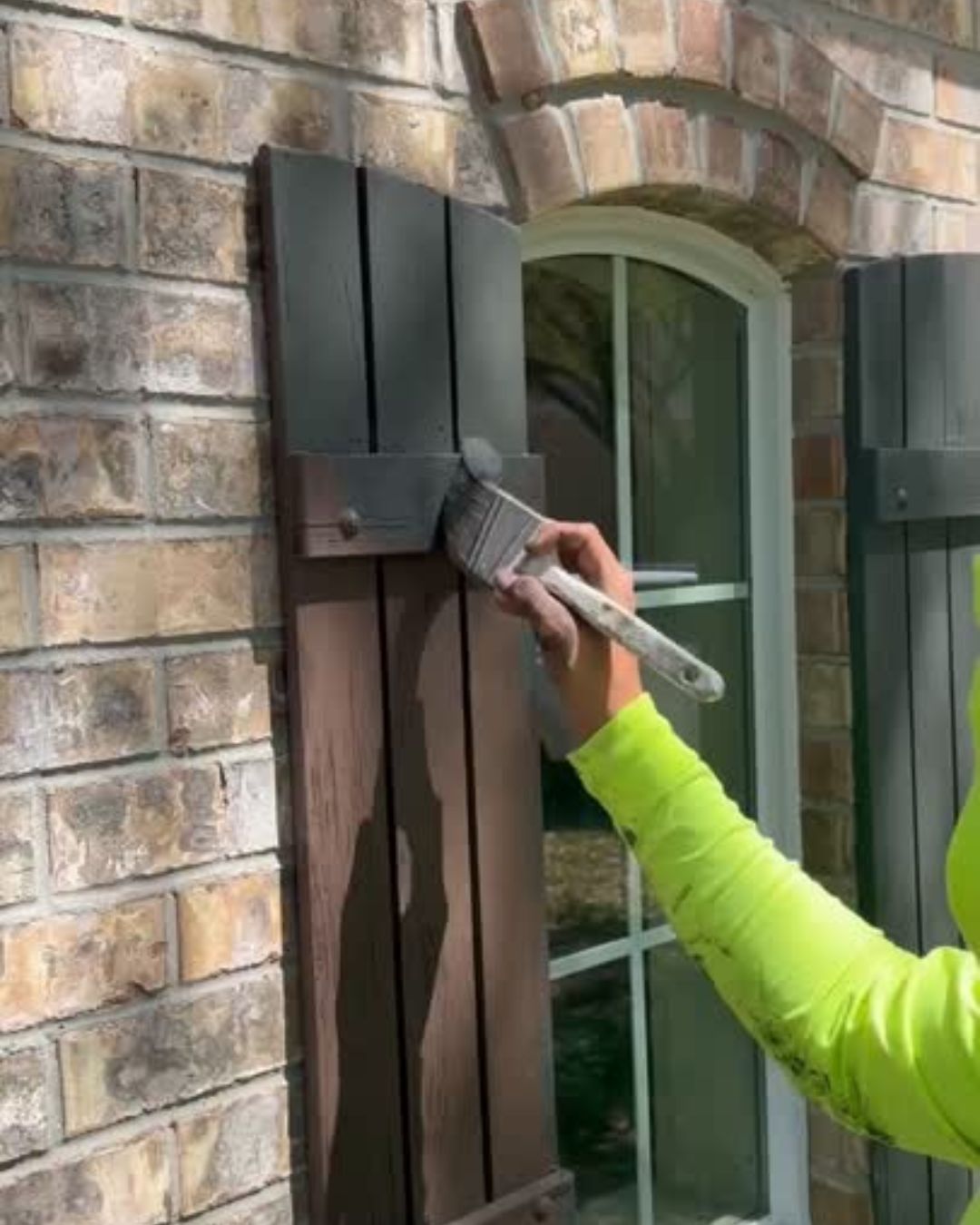 Painter applying finish to exterior shutters on brick home