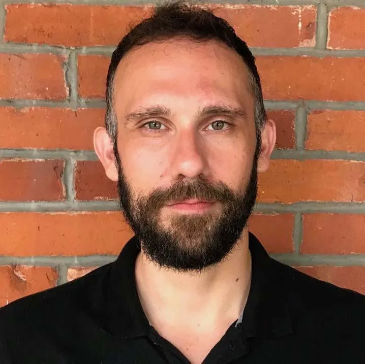 Photo of Gio Iacono in black shirt, standing in front of a red brick wall