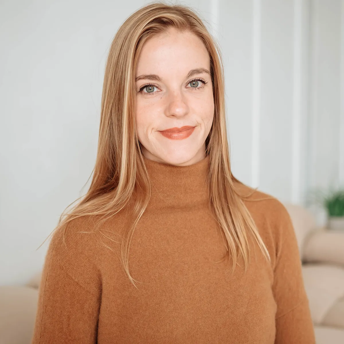 Photo of Haley Moore in a caramel knit turtleneck sweater in a white room with beige furniture in the background
