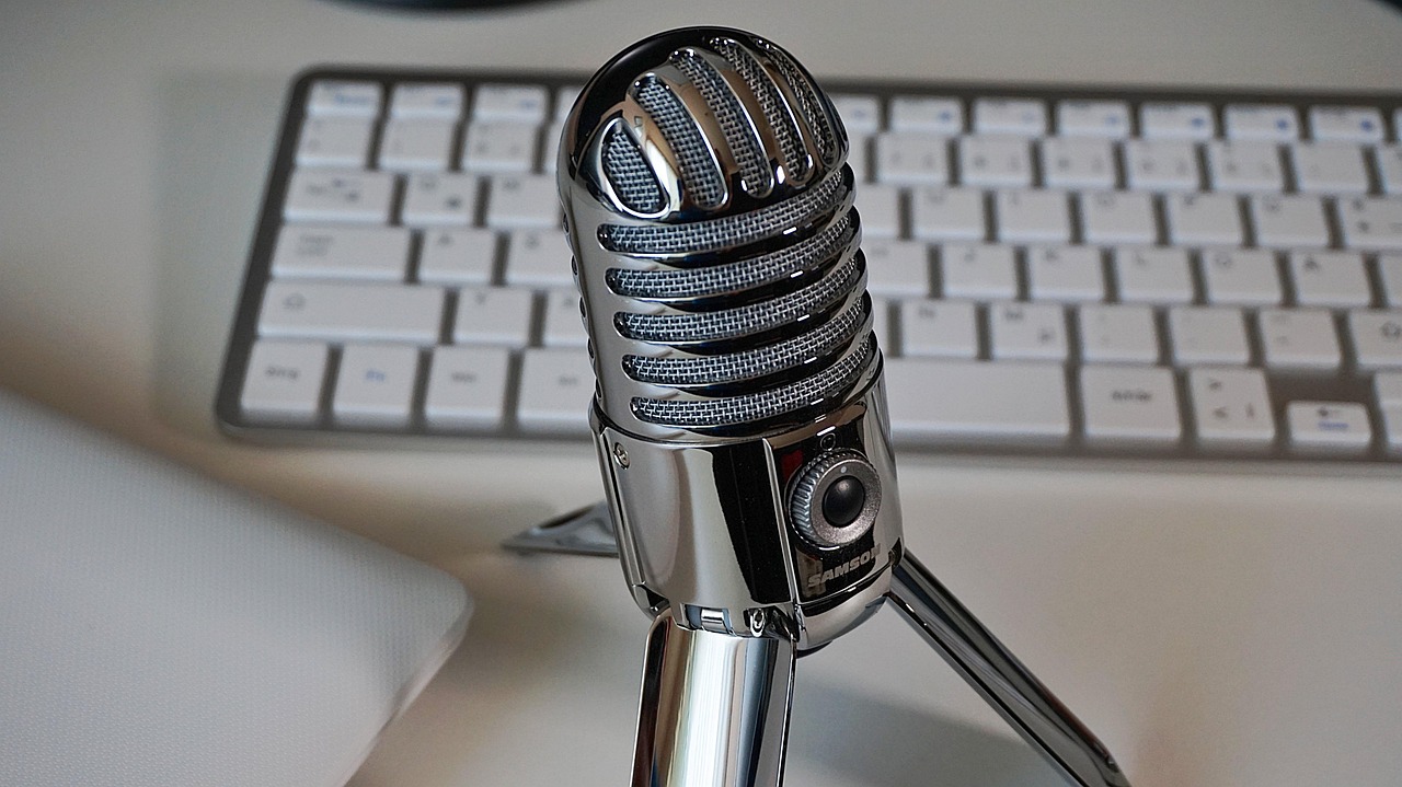 Silver microphone with a silver keyboard and a silver laptop on a white table