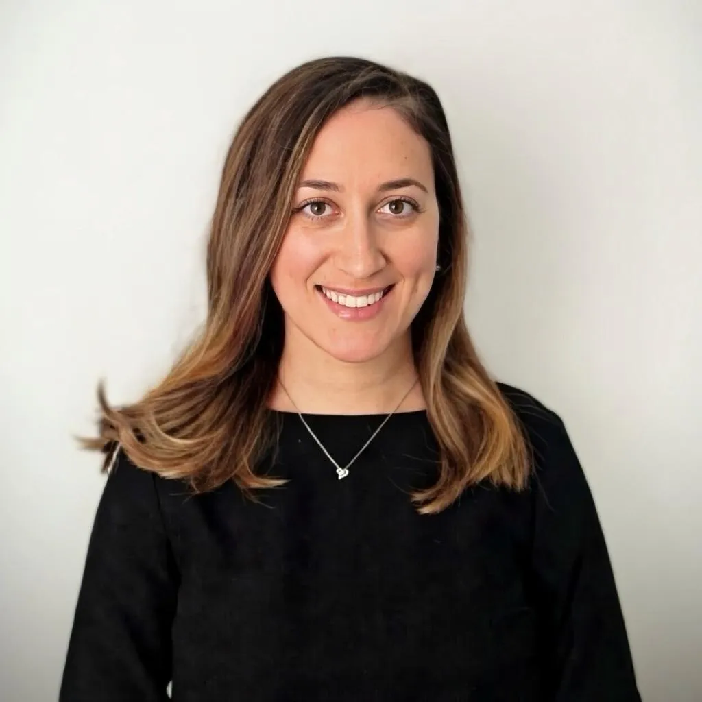 Photo of Sandra Borkovic in a black top wearing a dainty silver necklace, standing in front of a white wall