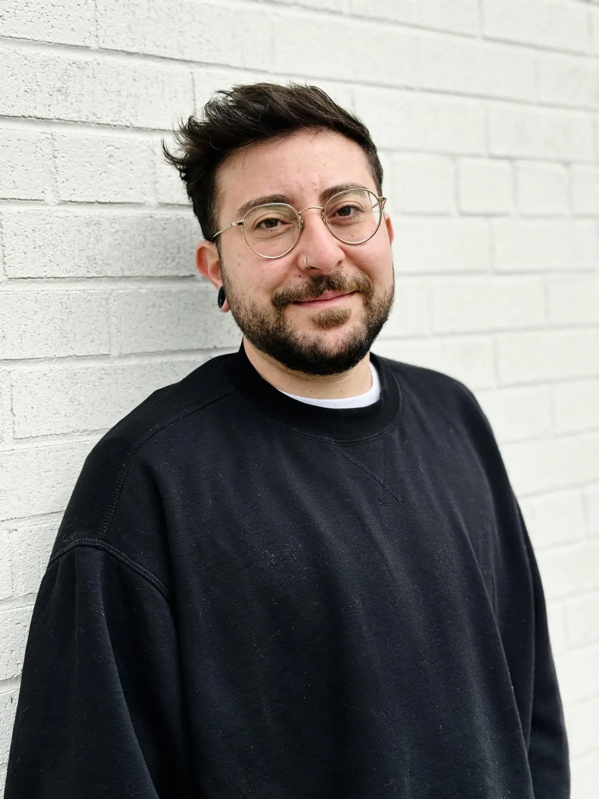Photo of Rayan Anton in a back sweatshirt, standing in front of a white brick wall