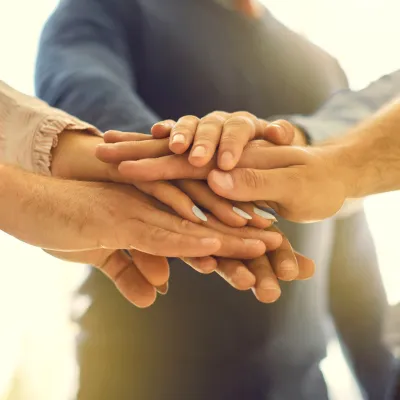 Stacked hands showing unity and teamwork, representing group coaching to transform and win together with Hyper-Ketosis.