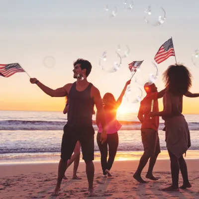 People waving flags on the beach at sunset during the 4th of July Freedom Weight Loss Challenge with Hyper-Ketosis.