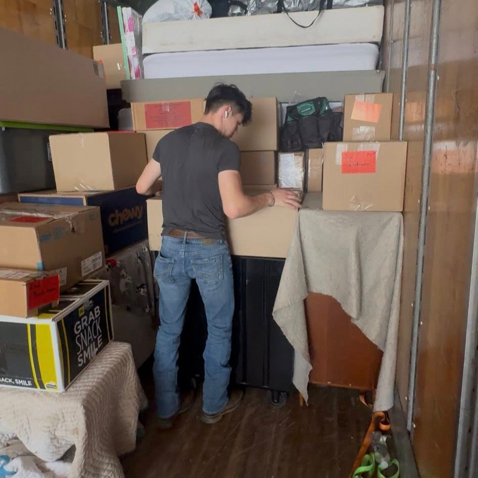 Two local movers wearing t-shirts that read 'Relocate Moving and Clean Out Company' while loading boxes into a truck
