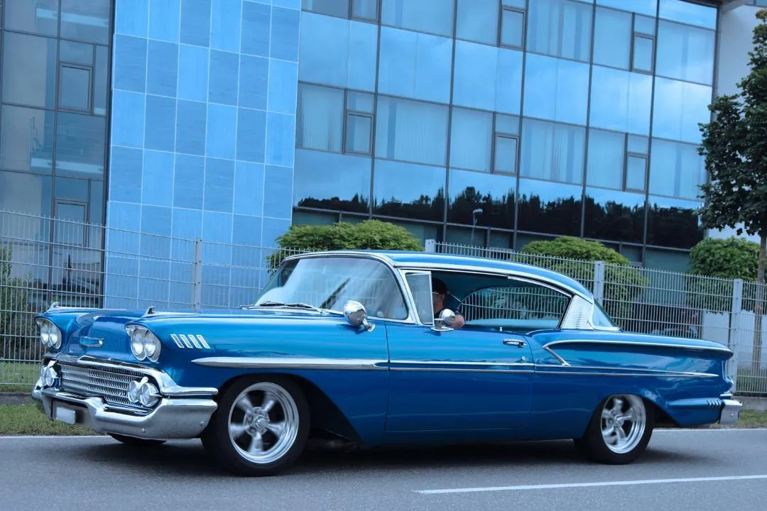 Blue vintage car driving through a city street, representing vehicles requiring emissions compliance and VIN verification in California.