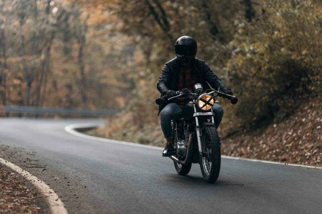 Motorcyclist riding through a winding forest road in autumn, illustrating steps to make a motorcycle street legal in New York.