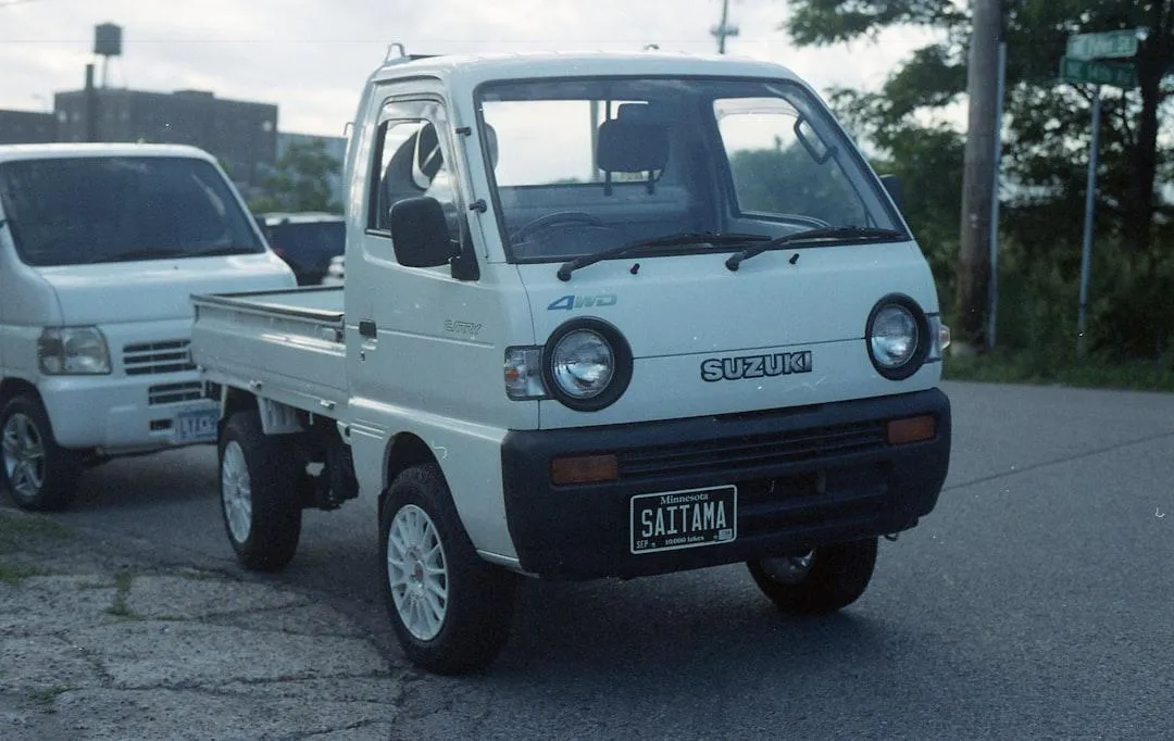 A white cab-over mini truck with a cargo bed and amber roof light.