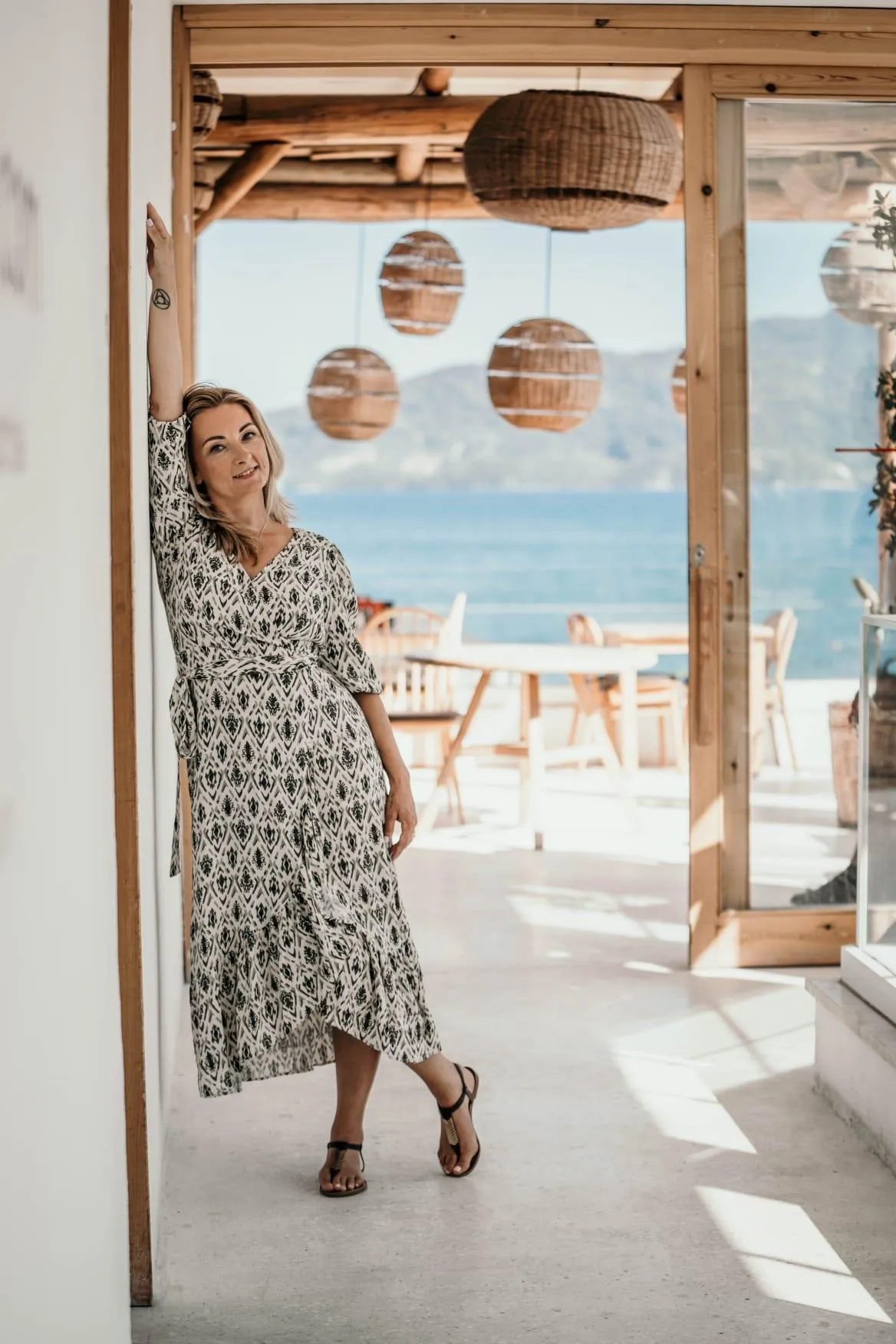 A confident woman in her 40s, standing in a sunlit studio, surrounded by soft pink and gold cosmic motifs, eyes closed in peaceful alignment, wearing modern business attire, radiating calm and empowerment. 3:2 aspect ratio.