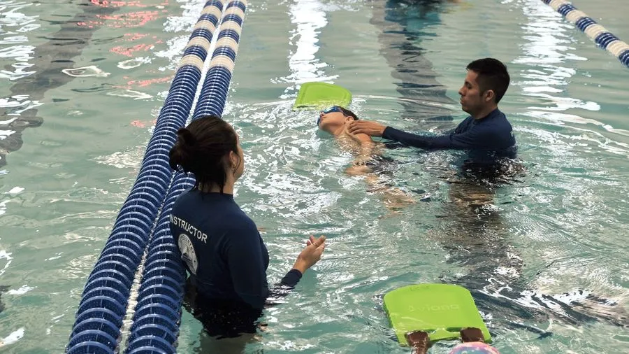 Instructors working with swimmers on kickboards between lane lines