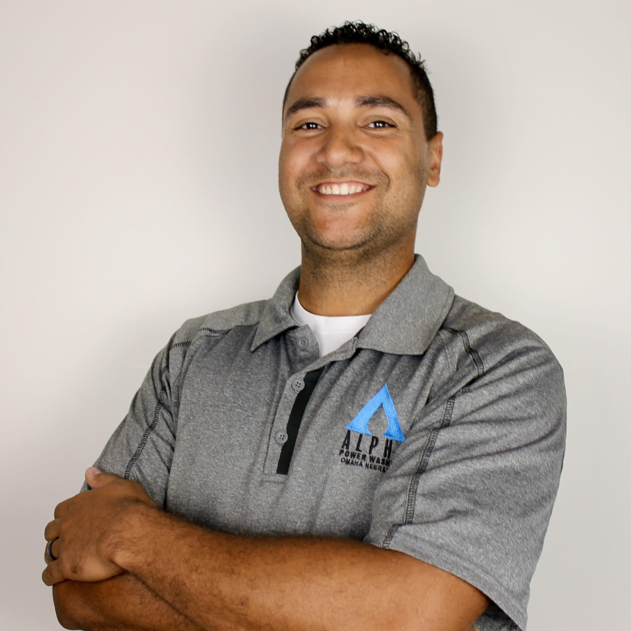 Professional exterior cleaner in uniform using a pressure washer on a brick walkway, with greenery and a home entrance in the background. The cleaner is focused and smiling, conveying trust and expertise.