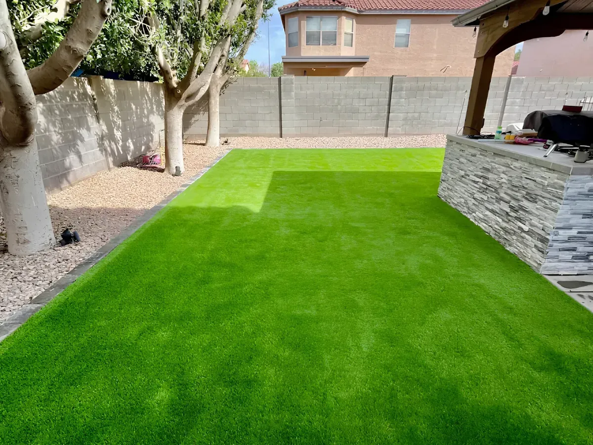 A modern backyard with artificial green turf, a small pool, and a covered patio under a blue sky.