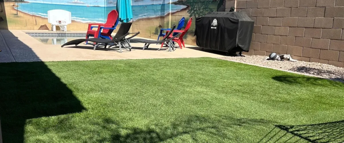 A backyardA modern backyard features artificial turf leading to a rectangular swimming pool with a waterfall, under a clear blue sky.featuring green artificial turf with concrete paving, lounge chairs, and a pool area in the background.