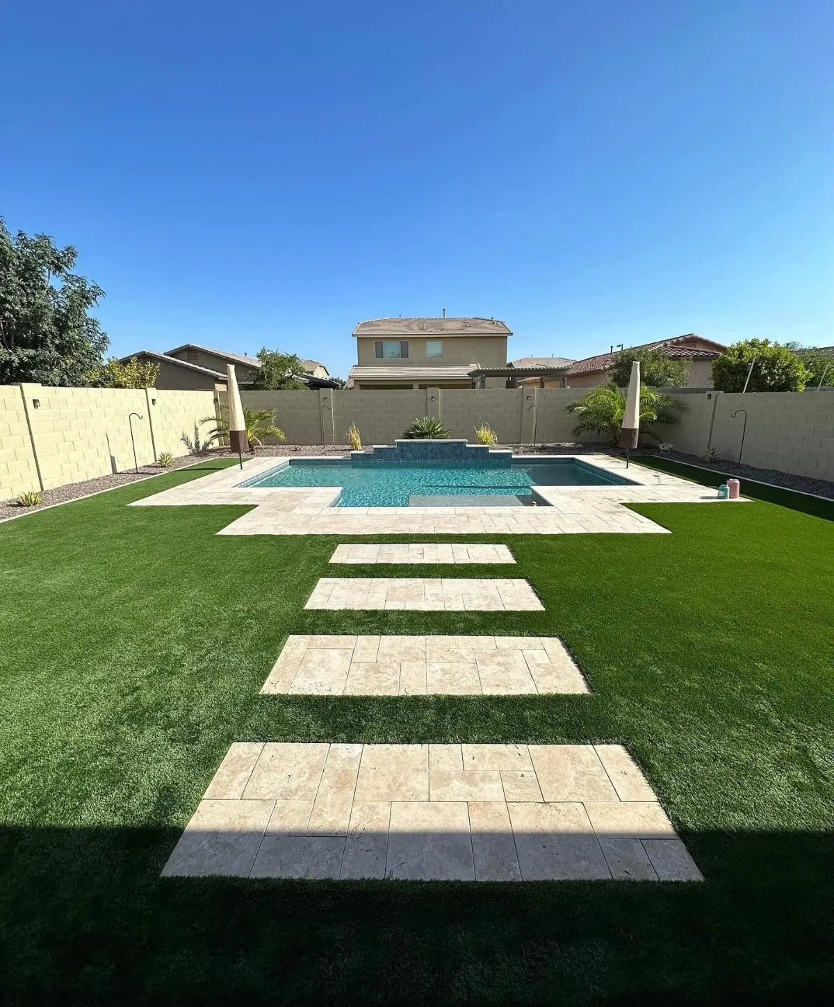 A backyard featuring artificial turf, a swimming pool with a painted mural, patio furniture, and a covered grill.