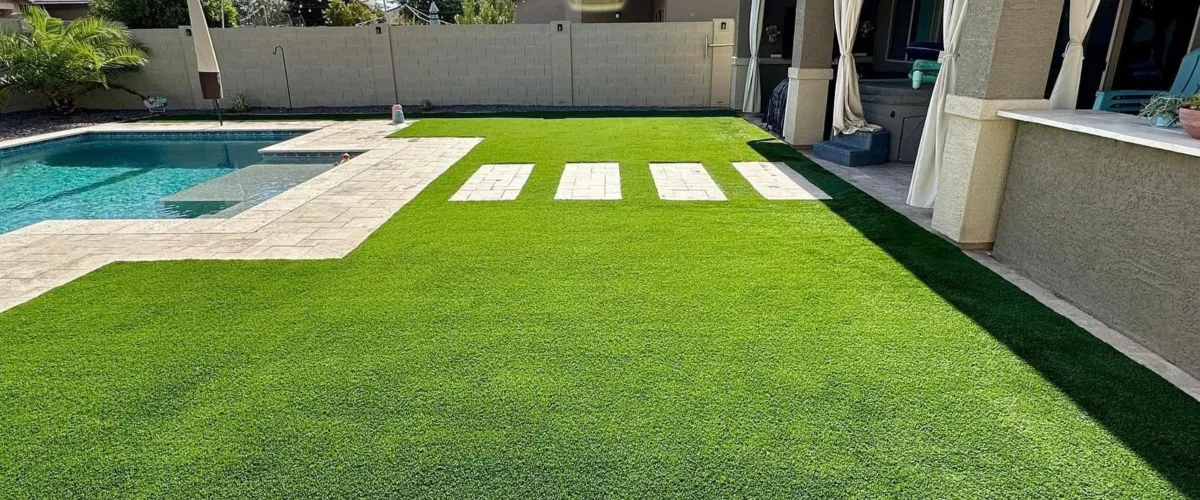 A luxurious backyard featuring a sparkling blue swimming pool, artificial green turf, and stepping stones leading to a patio.
