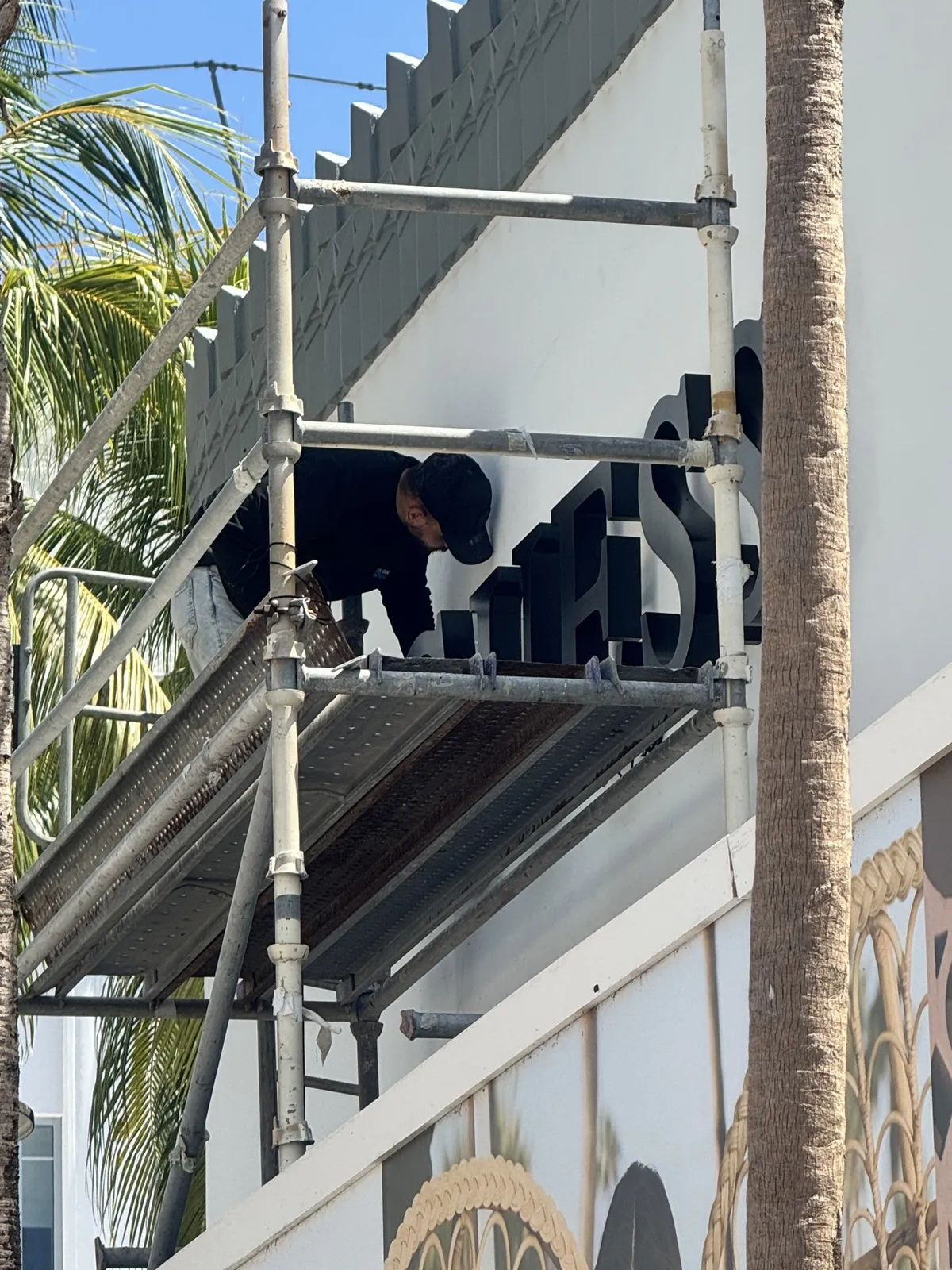 Crew installing black channel letters on a building from scaffolding, commercial sign installation Miami