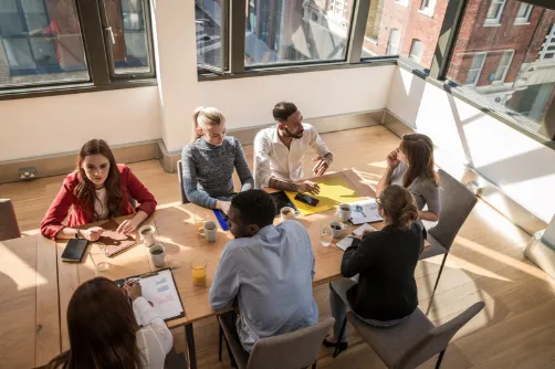 A team of colleagues meeting around a table in a bright workspace