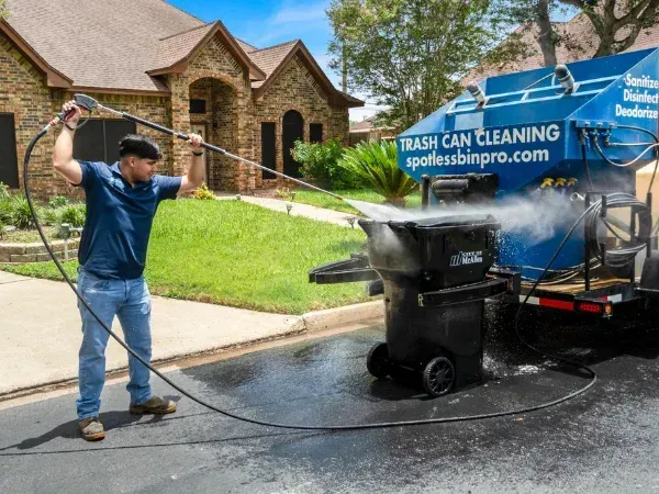 Trash bin cleaning truck lifting and spraying bin during cleaning process