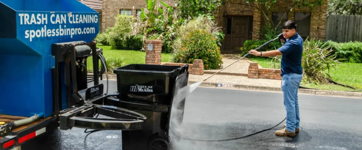 Residential trash bin being pressure washed curbside by cleaning technician