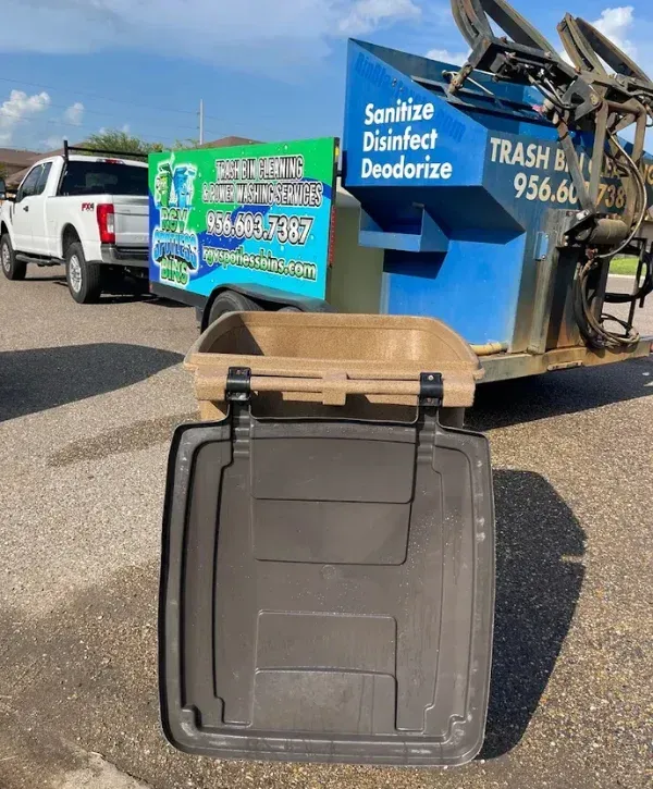 A BinBlast truck with a white pickup truck, a services trailer, and an open trash bin on an asphalt lot.