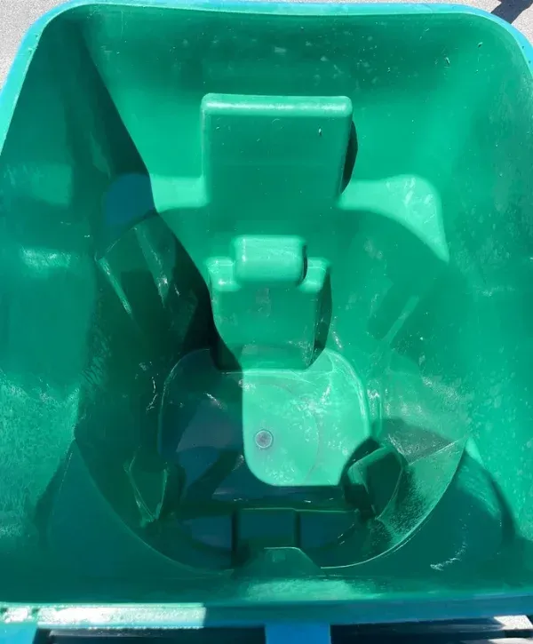 A clean, empty green plastic trash bin viewed from directly above, showing its interior details in bright sunlight.