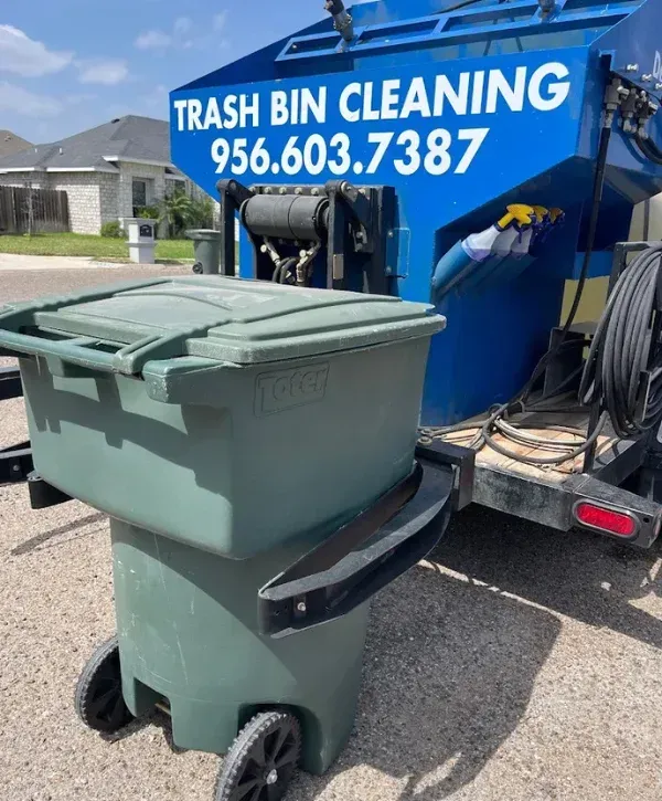 A green Toter trash bin attached to a blue trash bin cleaning service truck with a phone number on its side.