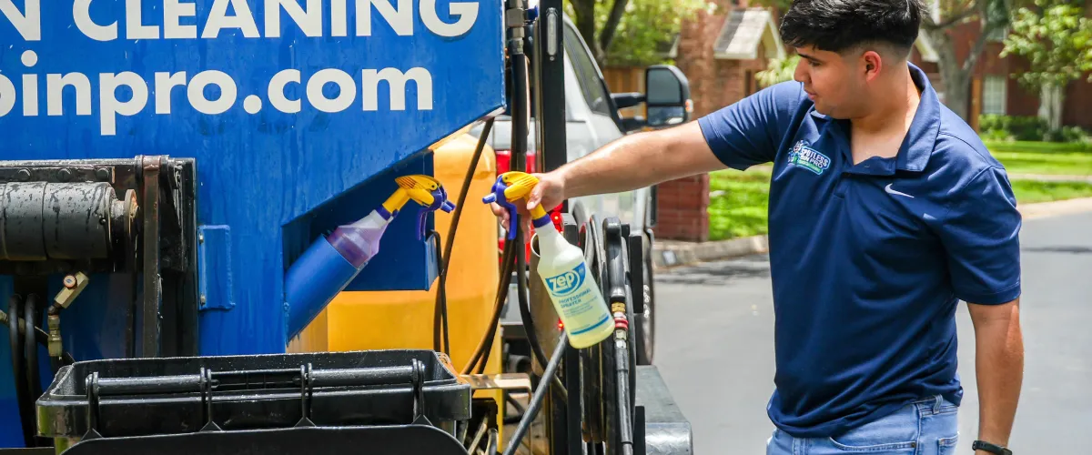 A commercial trailer for RGV Spotless Bins, a trash bin cleaning and power washing service, parked on a street near a house.