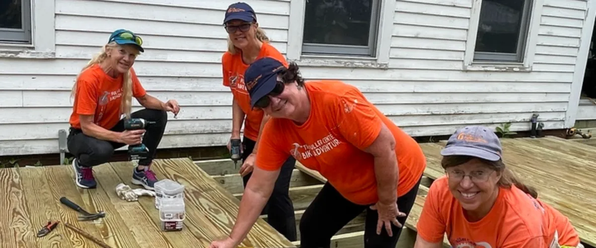 Four volunteers in orange Fuller Center shirts smiling while working on a deck build