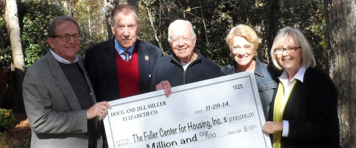 Jimmy Carter holding a donation check at a community fundraising event supporting affordable housing.