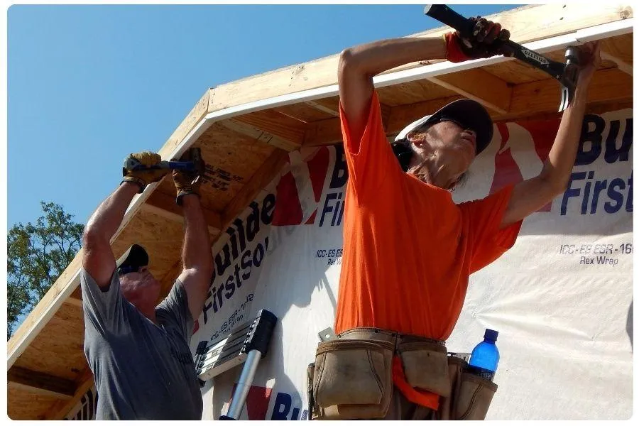 Volunteers hammering nails into wood framing during home construction
